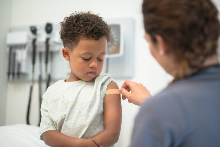 A boy looks down with caution as his doctor places a bandaid on his arm.