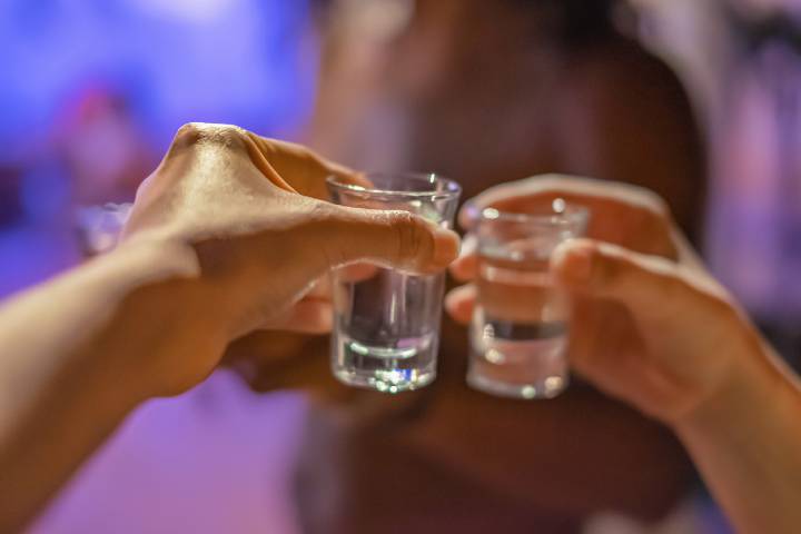 Close-up shot of two unrecognizable hands holding a tequilla shot at a birthday celebration. They're ready for a toast.