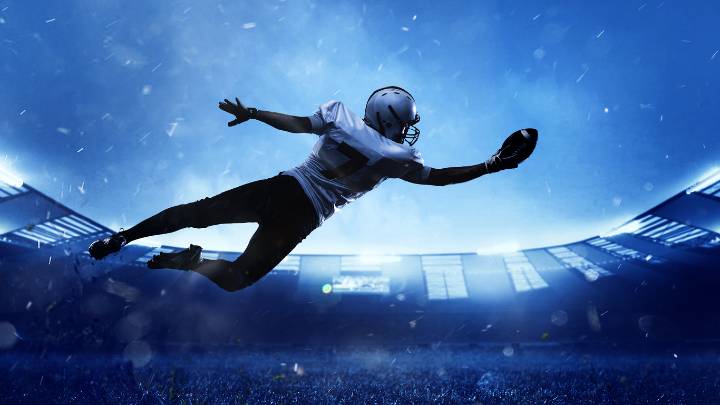 High jump. Professional American football player in motion, action during match at stadium. Sportsman in uniform catching ball. Concept of movement and action, sport lifestyle, competition