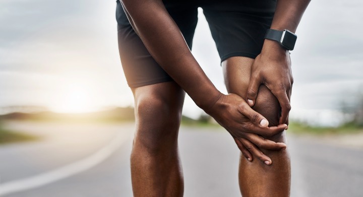 Closeup shot of a sporty man suffering with knee pain while exercising outdoors