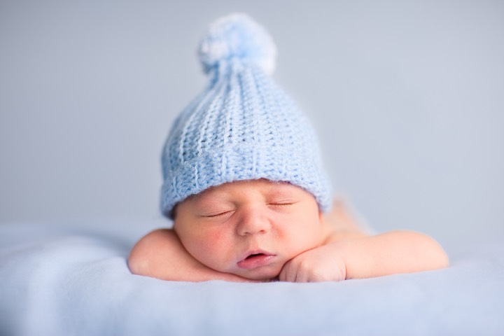 Color photo of a newborn baby boy sleeping peacefully while wearing a beanie hat.