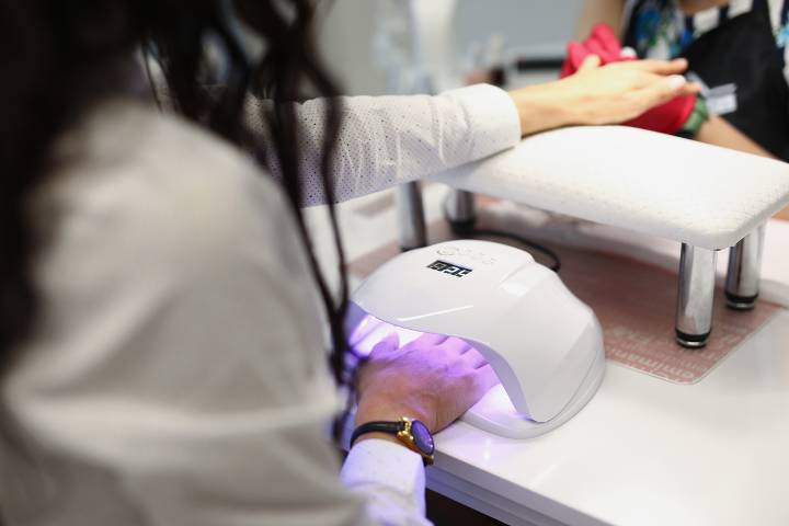 Close-up of manicurist covering nails of client with lights nail polish. Businesswoman preparing to meeting with colleagues. Beauty salon and personal care concept